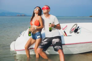 young couple leaning against boat with drinks in hand in shallow water.