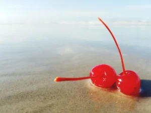 close up of two maraschino cherries in shallow beach water